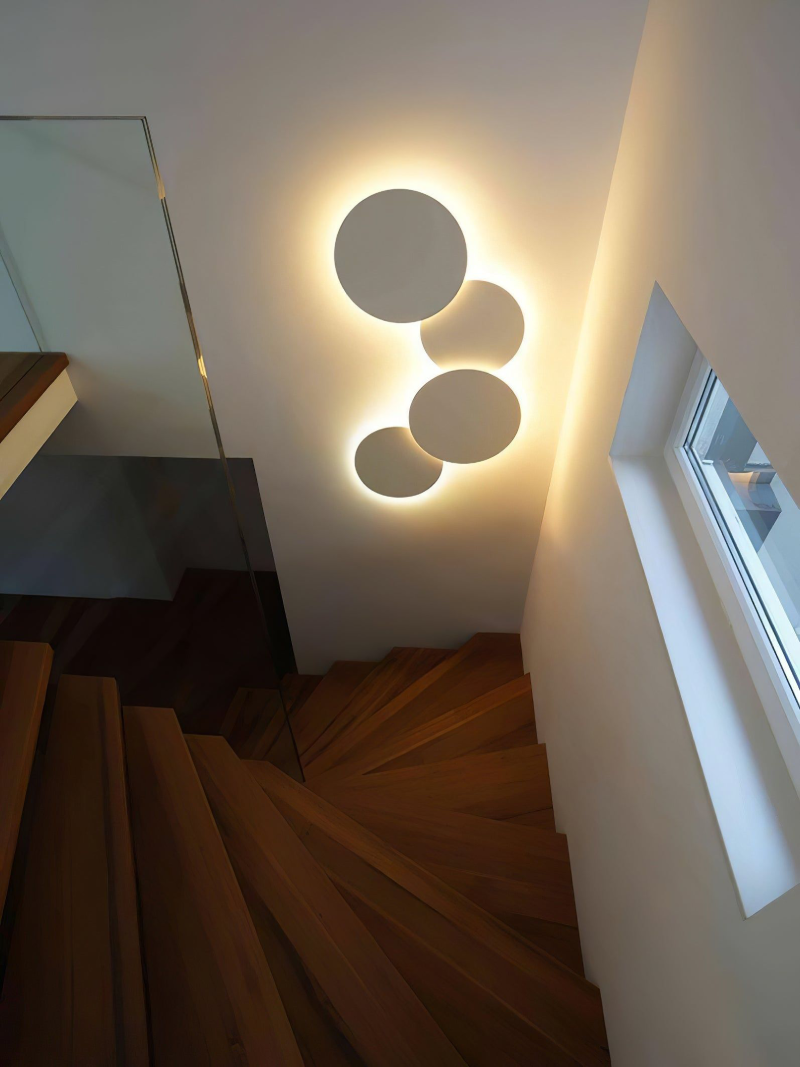 Những chiếc đèn hắt sáng hình tròn xếp nối tiếp nhau tạo thành bức tranh trang trí đầy duyên dáng nơi hông tường cầu thang